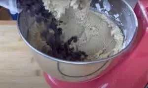 Mixing chocolate chips into cookie dough in a red stand mixer on a wooden surface.